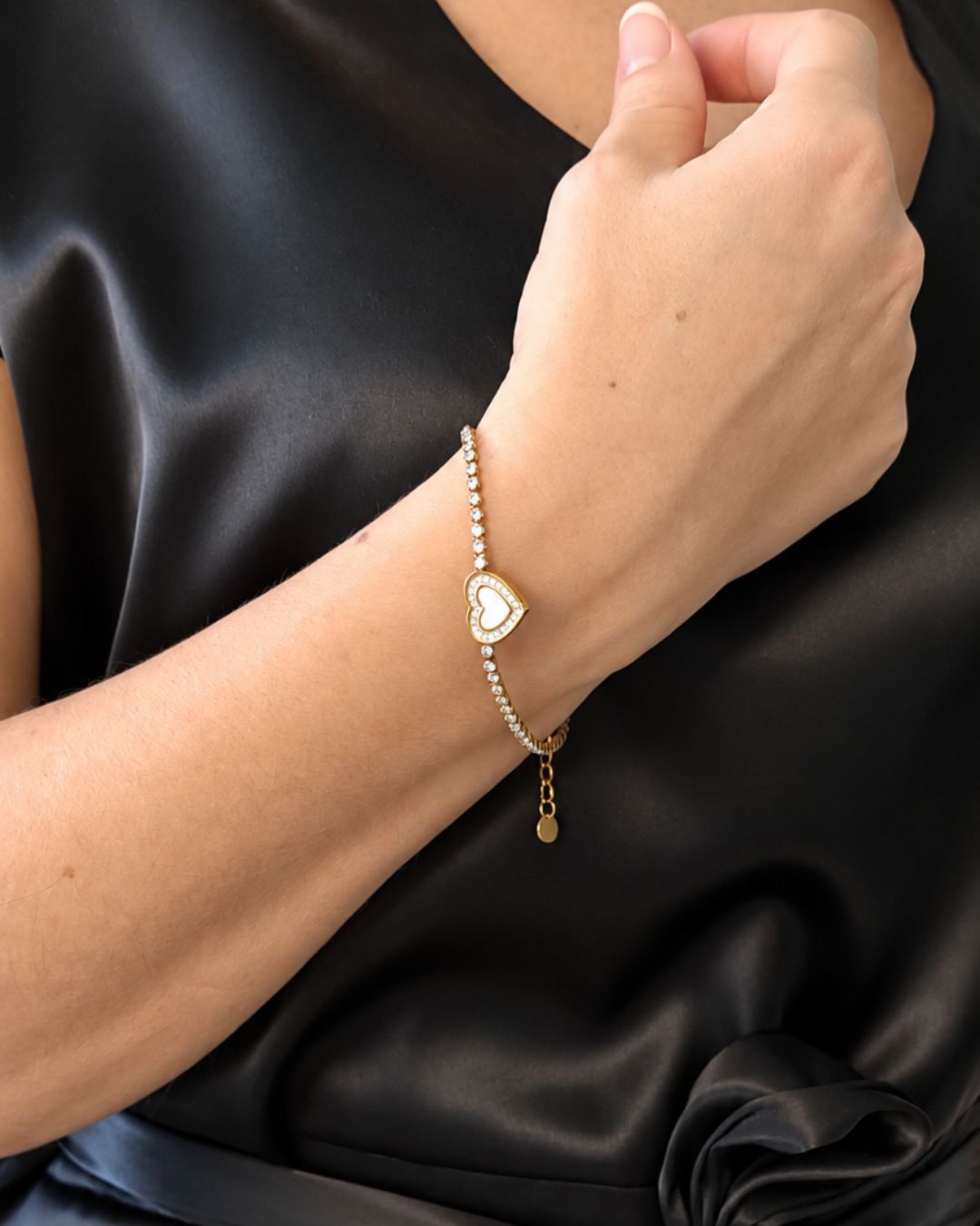 Woman wearing the Eternal Heart 18K gold PVD bracelet with an elegant black satin outfit, highlighting its sparkling stones and romantic heart design.