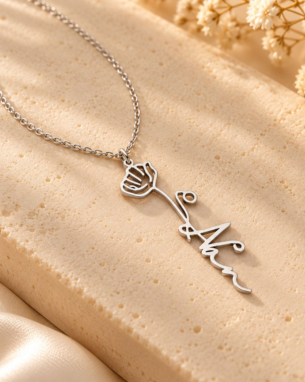 GIVERNY silver-tone personalised name necklace with a rose pendant on a beige surface