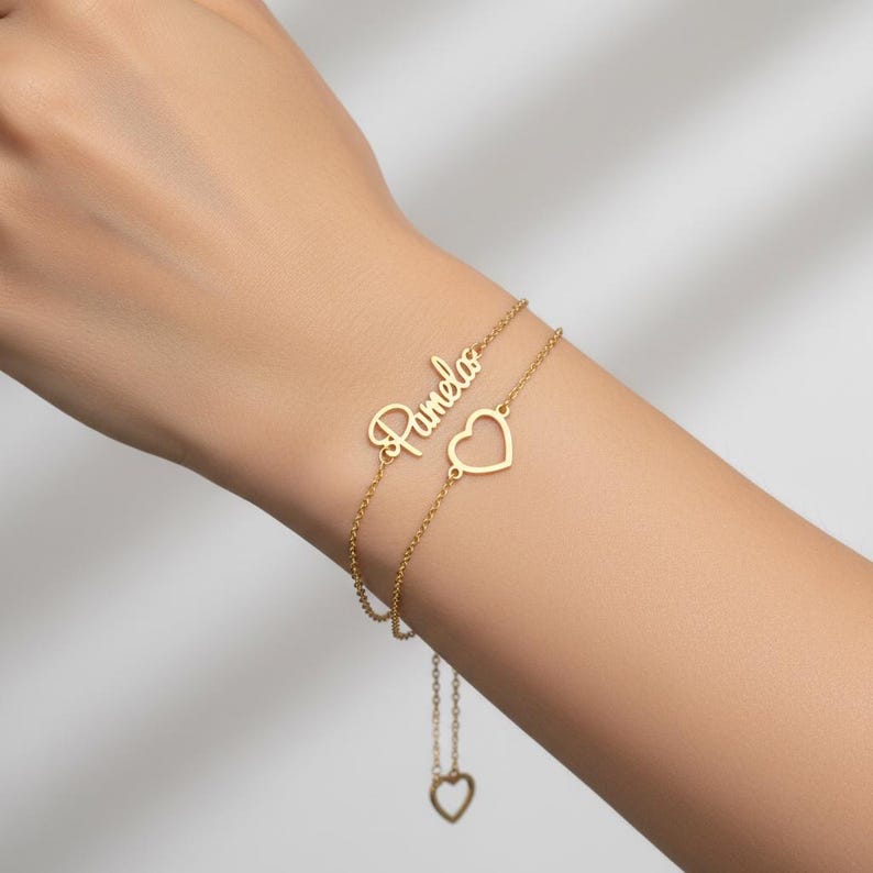 Close-up of the gold-finish Hope bracelet worn on a wrist, showing personalised lettering, two fine chains and an open heart.