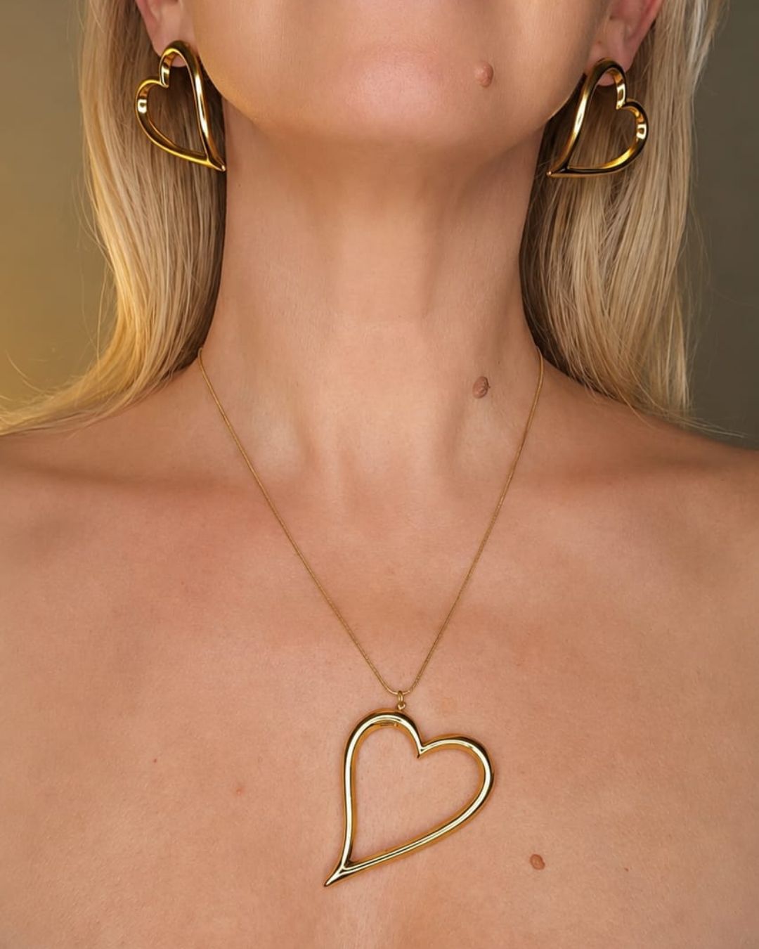 Woman wearing the gold-finish Love open-heart necklace and matching earrings, shown from the front.