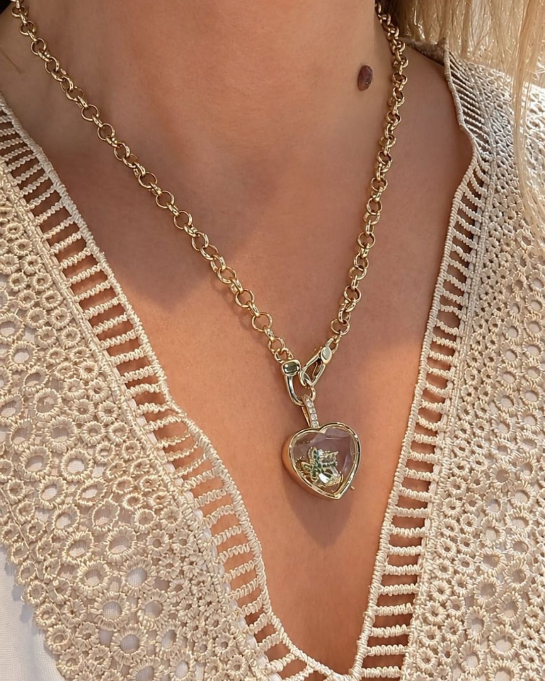 Collier Remember Locket Pendant doré avec médaillon en forme de cœur transparent, porté par une femme avec un haut en crochet beige.